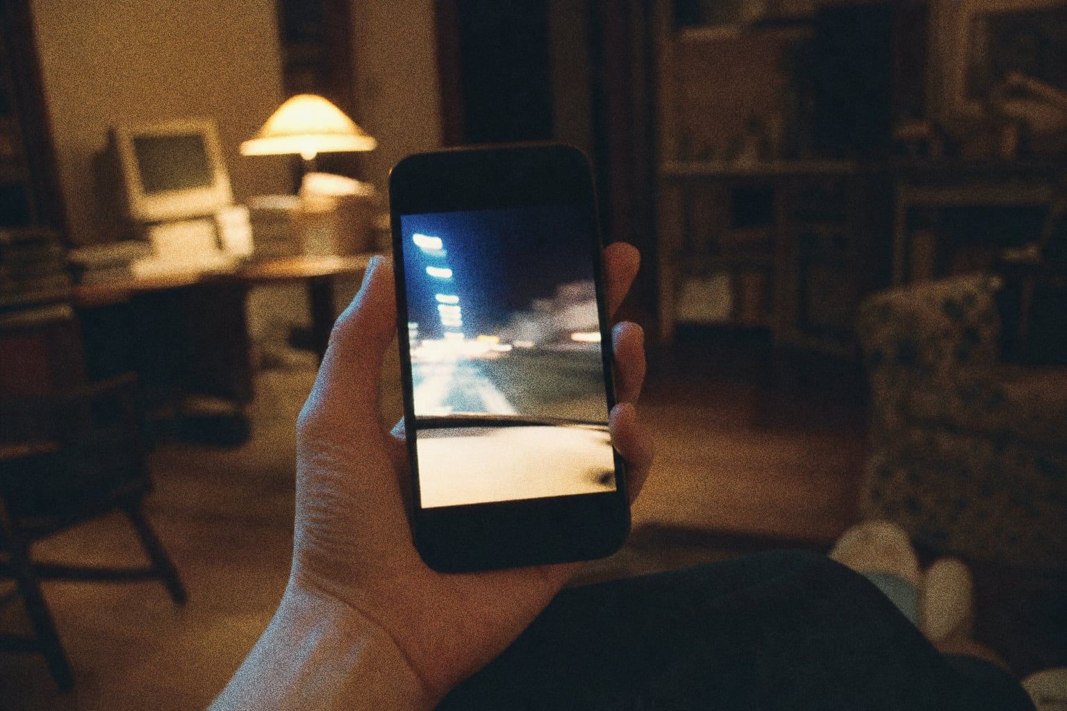 A hand holding a smartphone showing a vertical video, screen glowing in a dim room at night, shot on grainy film.
